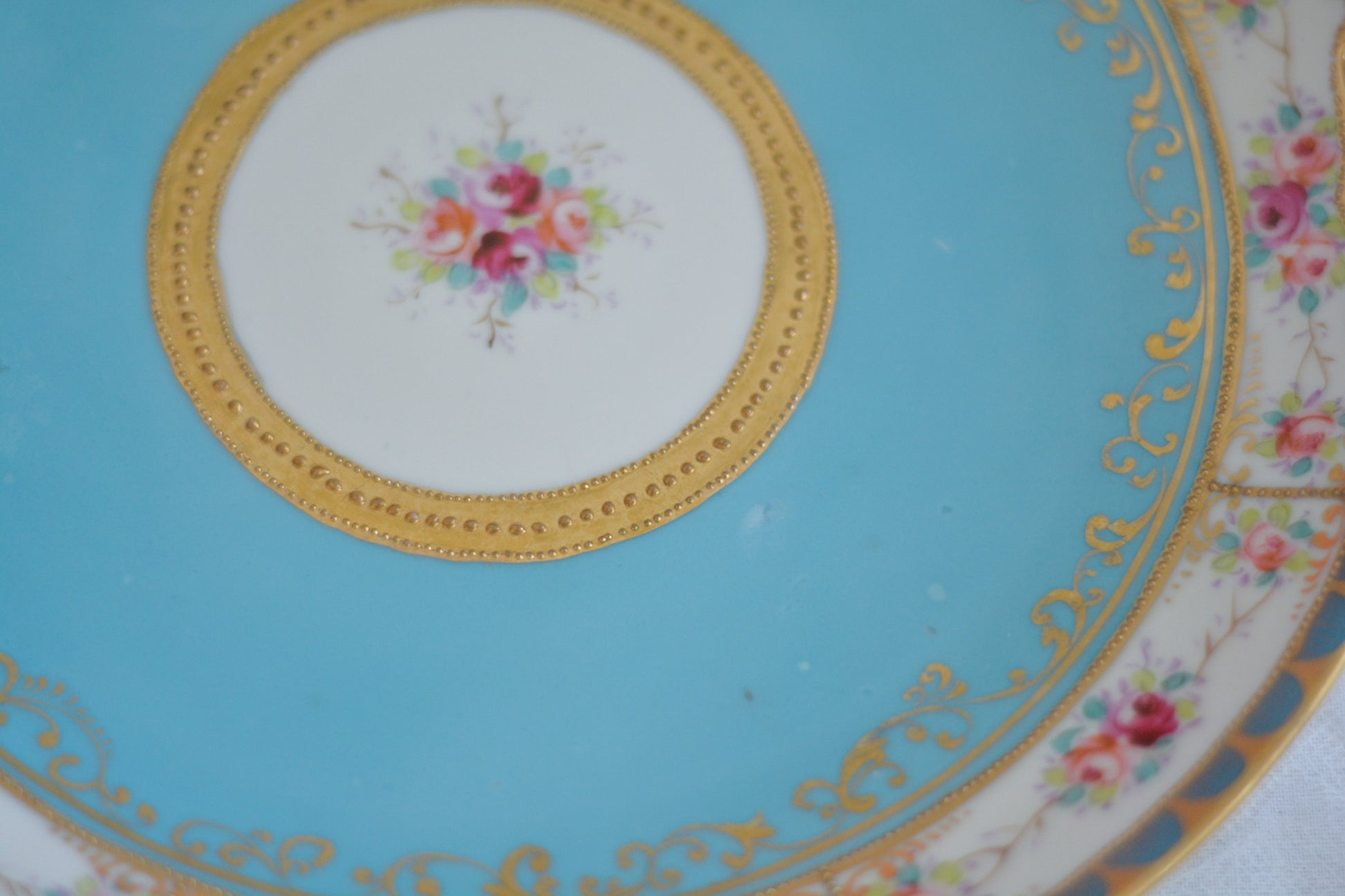 L&COという日本のメーカーのアンティーク里帰り品です。美しいターコイズブルーに金盛りの金彩、ハンドペイントで描かれた可憐なバラが上品なお品。1800年代後半頃からノリタケをはじめ日本からたくさんのメーカーが英国やアメリカに陶磁器を輸出していました。L&COは英国の老舗デパートリバティで販売されていたと言われています。キラキラしたティーセットやプレート達がデパートに並べられている風景は、当時の人々の目と心を楽しませていたことでしょう。