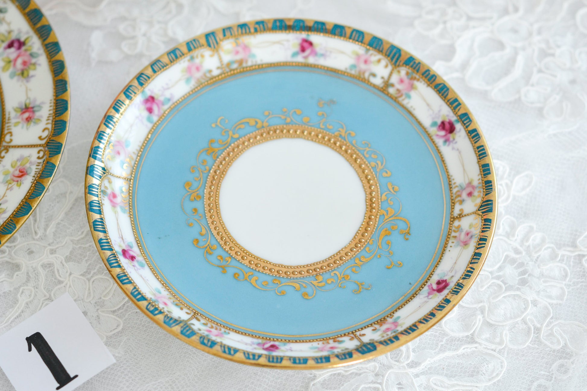 L&COという日本のメーカーのアンティーク里帰り品です。美しいターコイズブルーに金盛りの金彩、ハンドペイントで描かれた可憐なバラが上品なお品。1800年代後半頃からノリタケをはじめ日本からたくさんのメーカーが英国やアメリカに陶磁器を輸出していました。L&COは英国の老舗デパートリバティで販売されていたと言われています。キラキラしたティーセットがデパートに並べられている風景は、当時の人々の目と心を楽しませていたことでしょう。オールドニッポンの美しいティーカップでティータイムをお楽しみください。