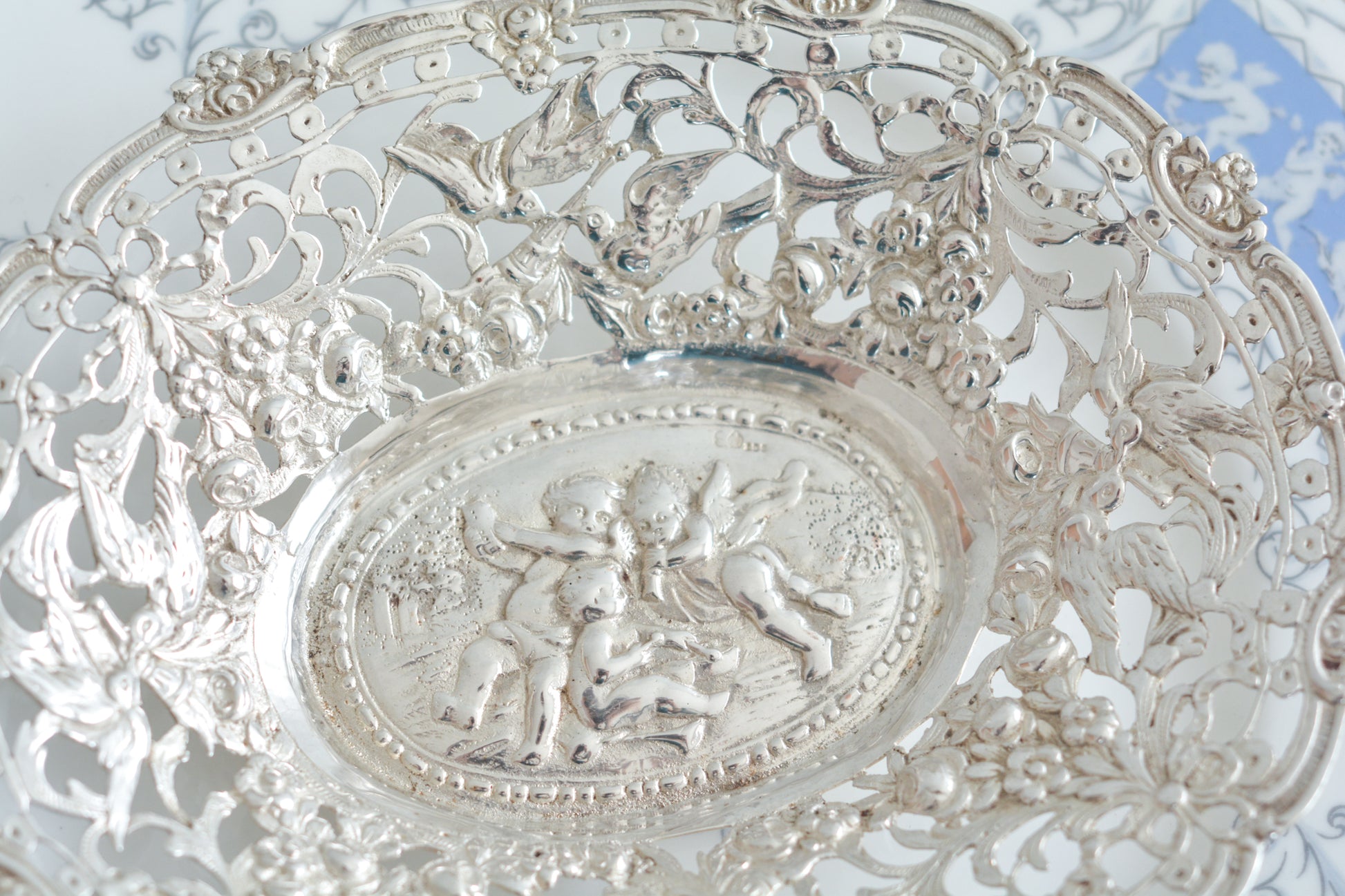 天使にリボンと薔薇のガーランドのピアス細工がとても愛らしく美しいボンボンディッシュです。 こちらはドイツで作られてイギリスに輸入されたお品です。繊細なピアス細工(透かし模様)に可愛らしい天使達がとても美しいお品です。ボンボンディッシュとはチョコレートやキャンディーなど小さなお菓子を入れて、ゲストがつまめるようにテーブルなどに置いておくためのお皿で、テーブルやお部屋に置かれていました。小ぶりなお皿で、ちょっとしたお菓子を乗せるのにぴったりです。