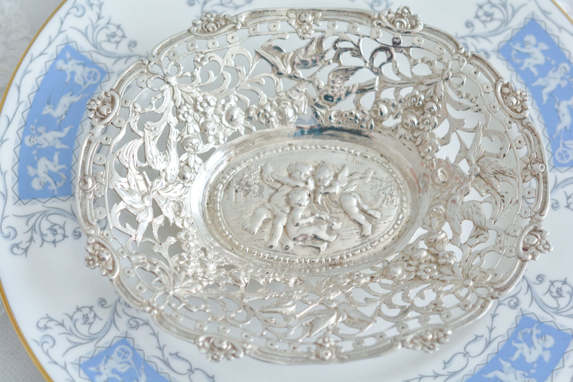 天使にリボンと薔薇のガーランドのピアス細工がとても愛らしく美しいボンボンディッシュです。 こちらはドイツで作られてイギリスに輸入されたお品です。繊細なピアス細工(透かし模様)に可愛らしい天使達がとても美しいお品です。ボンボンディッシュとはチョコレートやキャンディーなど小さなお菓子を入れて、ゲストがつまめるようにテーブルなどに置いておくためのお皿で、テーブルやお部屋に置かれていました。小ぶりなお皿で、ちょっとしたお菓子を乗せるのにぴったりです。