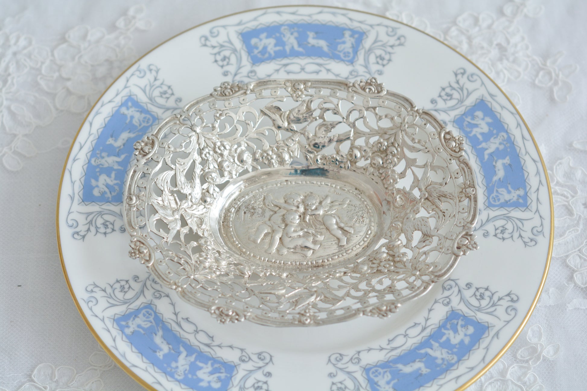 天使にリボンと薔薇のガーランドのピアス細工がとても愛らしく美しいボンボンディッシュです。 こちらはドイツで作られてイギリスに輸入されたお品です。繊細なピアス細工(透かし模様)に可愛らしい天使達がとても美しいお品です。ボンボンディッシュとはチョコレートやキャンディーなど小さなお菓子を入れて、ゲストがつまめるようにテーブルなどに置いておくためのお皿で、テーブルやお部屋に置かれていました。小ぶりなお皿で、ちょっとしたお菓子を乗せるのにぴったりです。