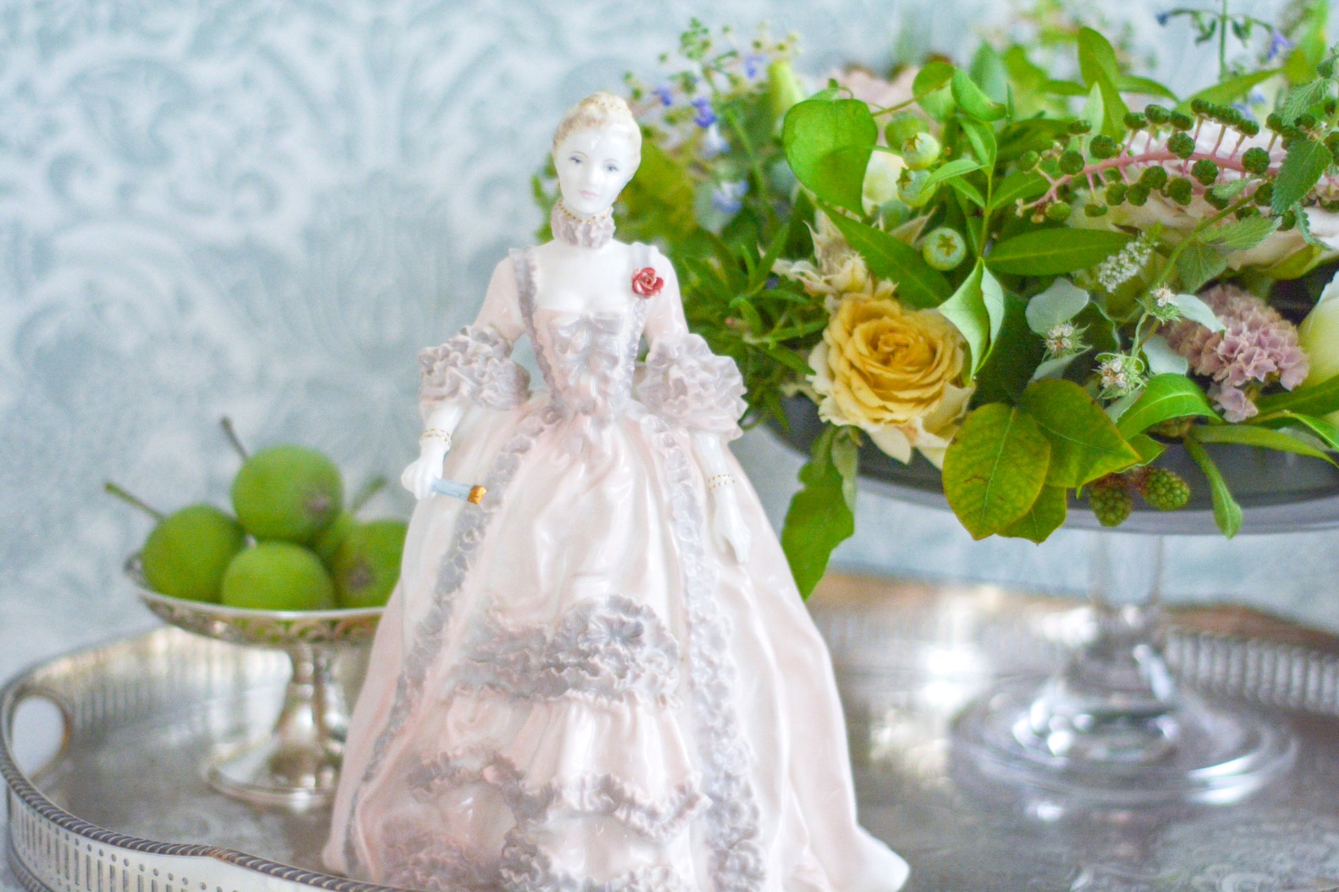 コールポートのポンパドール夫人の美しいフィギュリン。コールポートの中でも一番貴重で人気のフィギュリンではないでしょうか。美しいお顔にグレーとピンクの華やかなドレス。人気があるのも分かります。ポンパドール夫人はその美顔からフランスルイ15世の公式の愛妾となったのは有名な話。美顔だけでなく、頭もとてもよく政治にも積極的に関与しています。色々な側面を持ち合わせますが、芸術を愛し、その発展に大きな影響を与えました。ポンパドール夫人の時代はフランスを中心に優美なロココ様式が流行します。イギリスで1810年〜1830年代頃に流行したロココリバイバルはフランスのロココ様式の影響を受けてイギリスでロココ様式が再流行したものです。そんなポンパドール夫人のフィギュリンは、キャビネットに飾ってもティータイムにテーブルに置いてもどんなシーンでも、パッとスポットライトが当たったかのような存在感です。