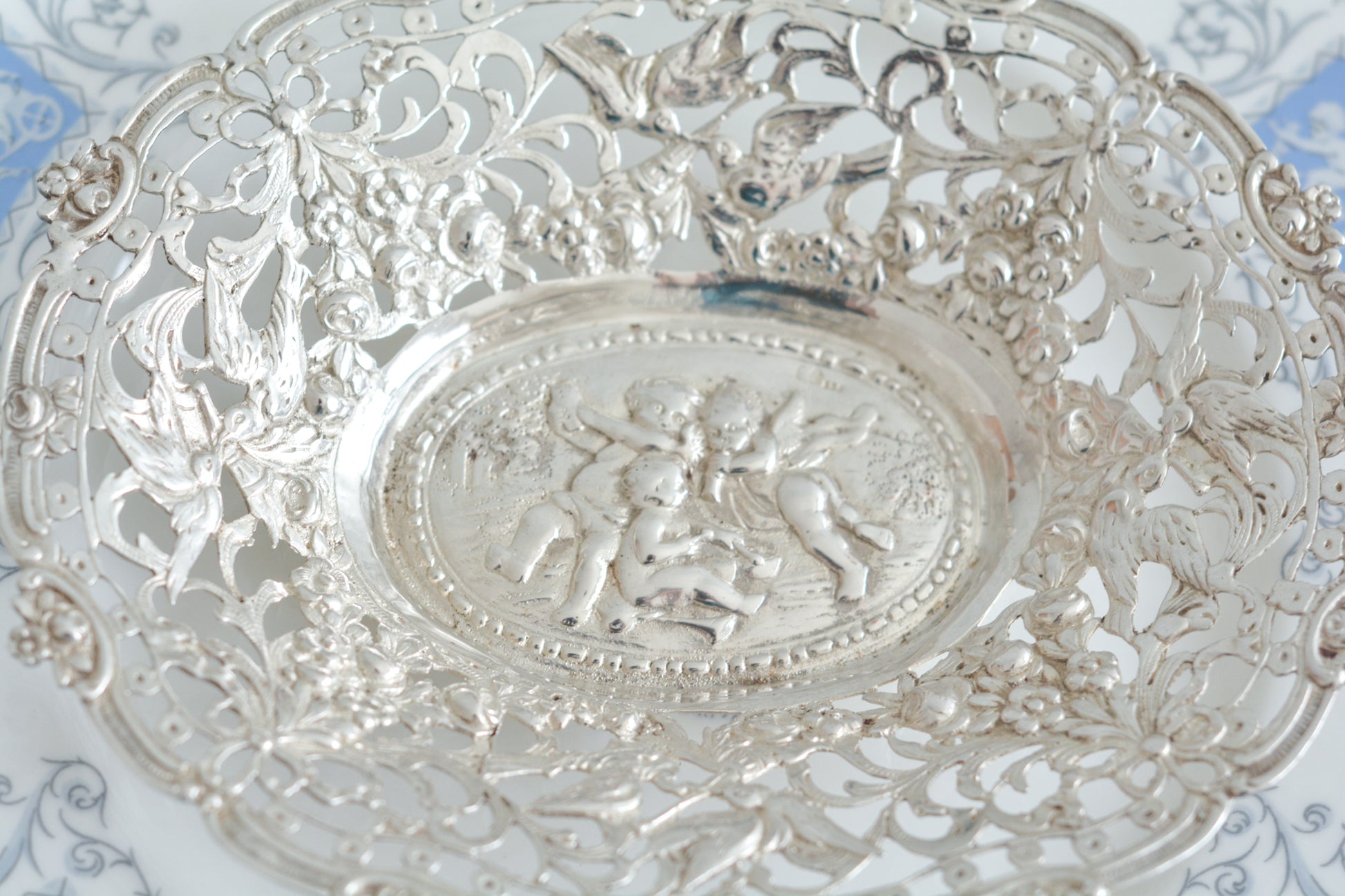 天使にリボンと薔薇のガーランドのピアス細工がとても愛らしく美しいボンボンディッシュです。 こちらはドイツで作られてイギリスに輸入されたお品です。繊細なピアス細工(透かし模様)に可愛らしい天使達がとても美しいお品です。ボンボンディッシュとはチョコレートやキャンディーなど小さなお菓子を入れて、ゲストがつまめるようにテーブルなどに置いておくためのお皿で、テーブルやお部屋に置かれていました。小ぶりなお皿で、ちょっとしたお菓子を乗せるのにぴったりです。