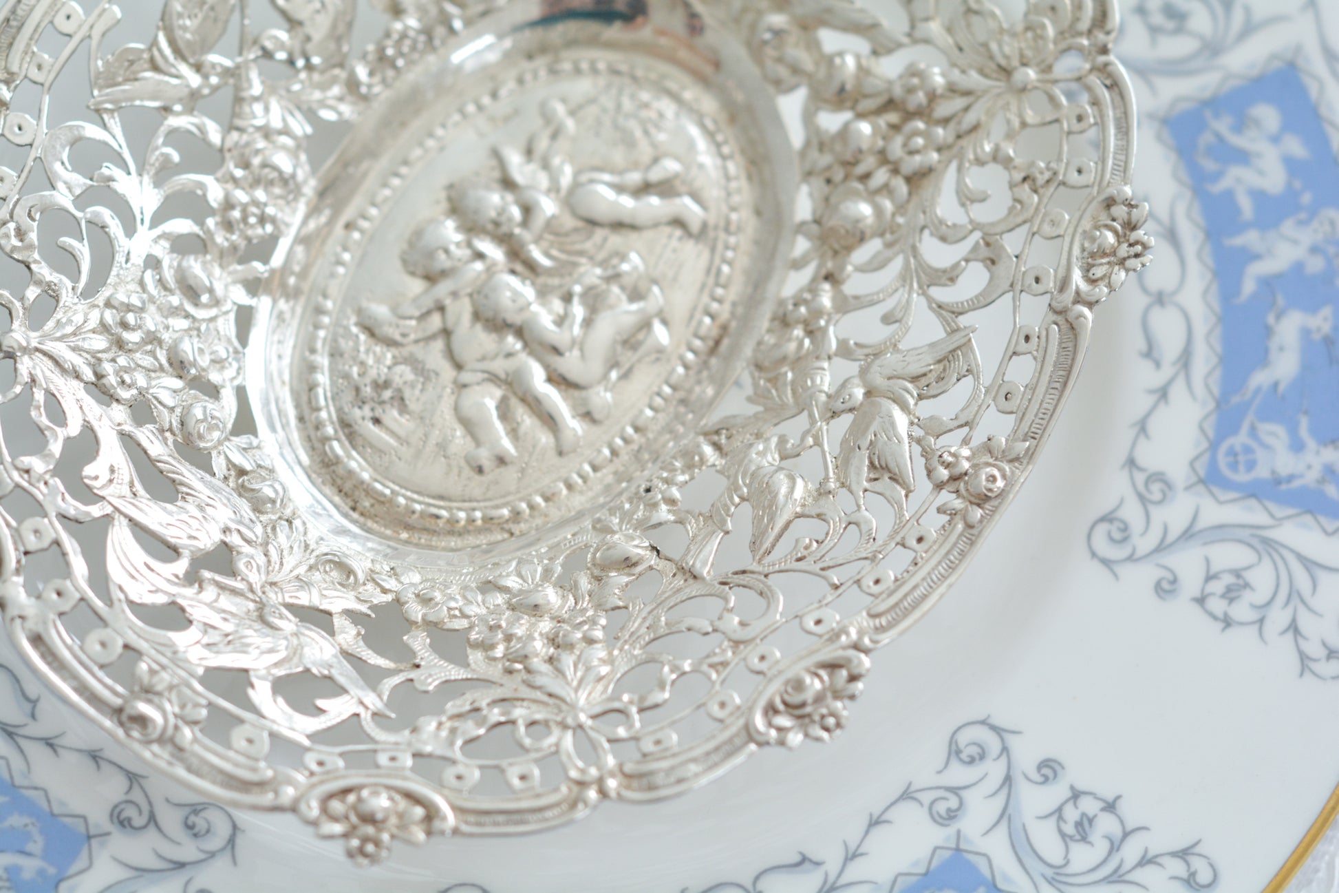 天使にリボンと薔薇のガーランドのピアス細工がとても愛らしく美しいボンボンディッシュです。 こちらはドイツで作られてイギリスに輸入されたお品です。繊細なピアス細工(透かし模様)に可愛らしい天使達がとても美しいお品です。ボンボンディッシュとはチョコレートやキャンディーなど小さなお菓子を入れて、ゲストがつまめるようにテーブルなどに置いておくためのお皿で、テーブルやお部屋に置かれていました。小ぶりなお皿で、ちょっとしたお菓子を乗せるのにぴったりです。