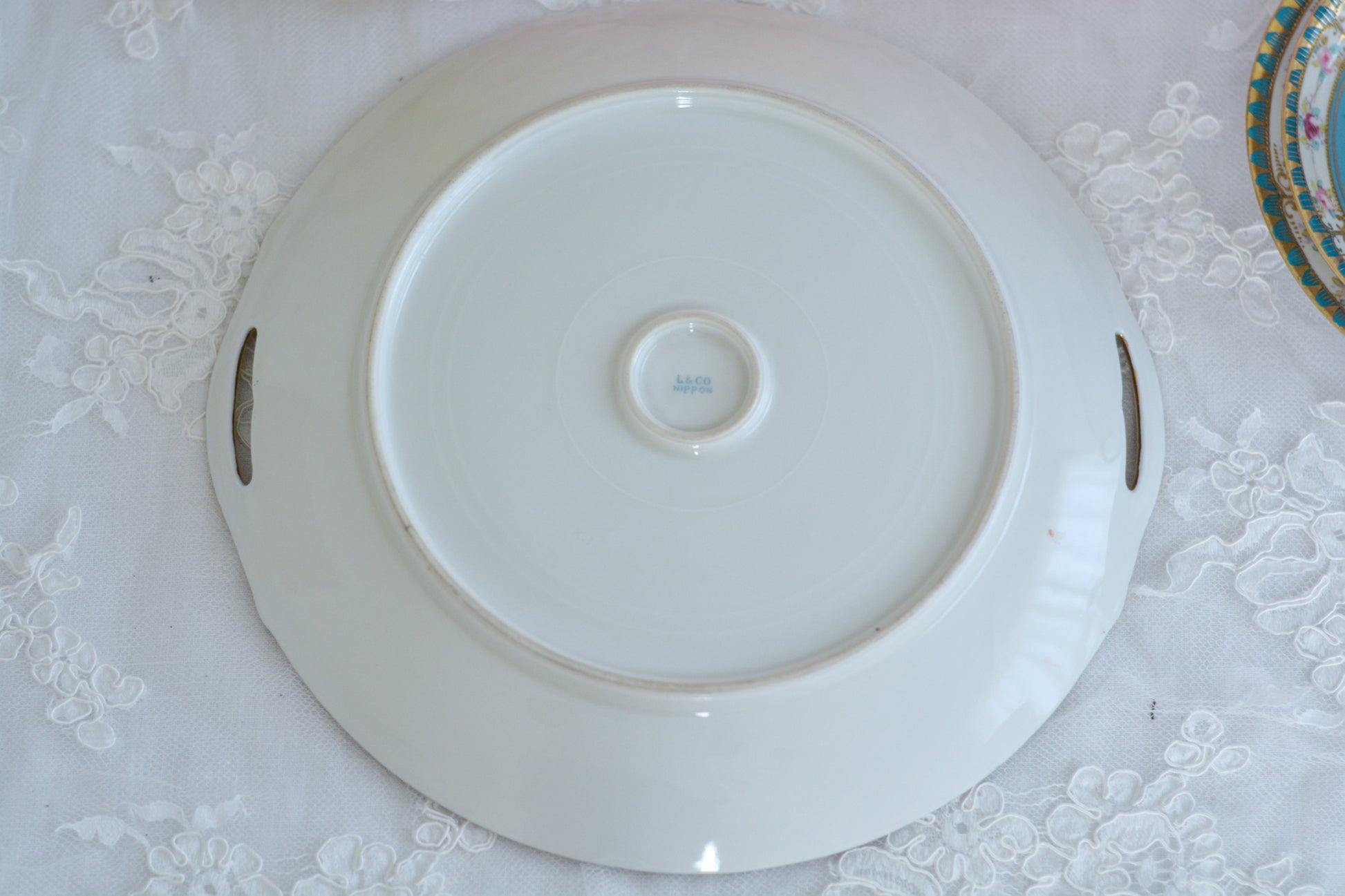 L&COという日本のメーカーのアンティーク里帰り品です。美しいターコイズブルーに金盛りの金彩、ハンドペイントで描かれた可憐なバラが上品なお品。1800年代後半頃からノリタケをはじめ日本からたくさんのメーカーが英国やアメリカに陶磁器を輸出していました。L&COは英国の老舗デパートリバティで販売されていたと言われています。キラキラしたティーセットやプレート達がデパートに並べられている風景は、当時の人々の目と心を楽しませていたことでしょう。