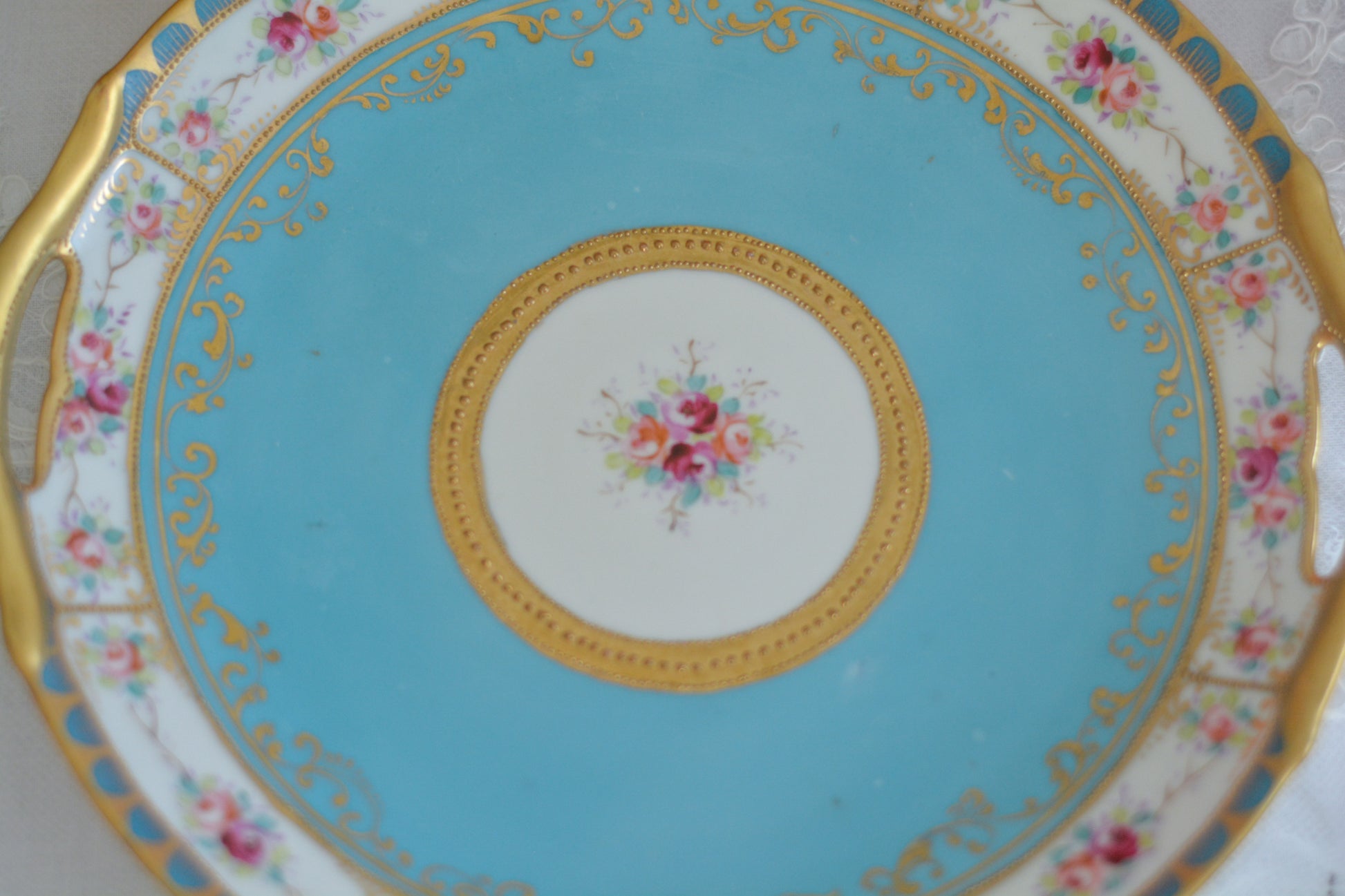 L&COという日本のメーカーのアンティーク里帰り品です。美しいターコイズブルーに金盛りの金彩、ハンドペイントで描かれた可憐なバラが上品なお品。1800年代後半頃からノリタケをはじめ日本からたくさんのメーカーが英国やアメリカに陶磁器を輸出していました。L&COは英国の老舗デパートリバティで販売されていたと言われています。キラキラしたティーセットやプレート達がデパートに並べられている風景は、当時の人々の目と心を楽しませていたことでしょう。