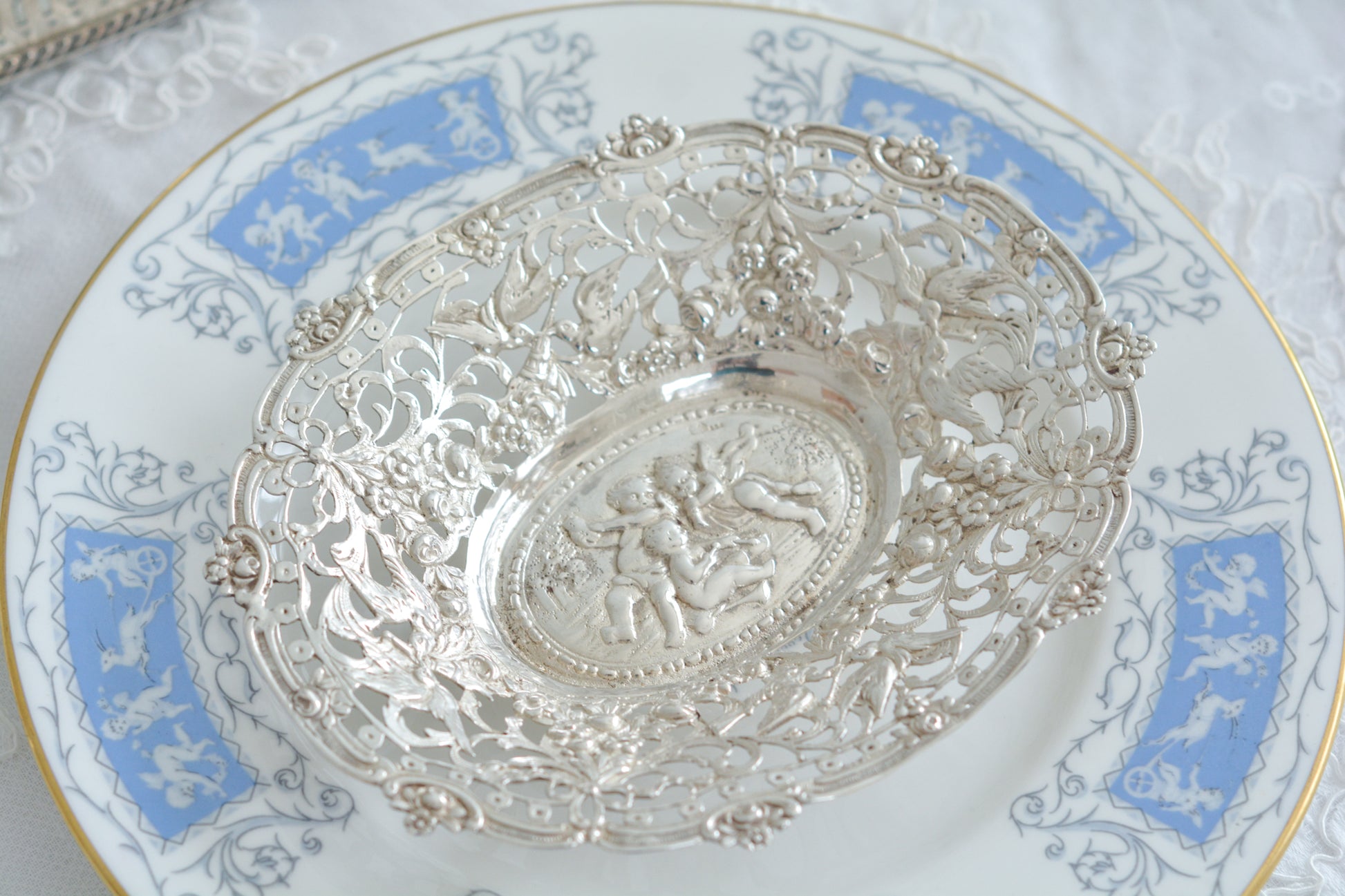 天使にリボンと薔薇のガーランドのピアス細工がとても愛らしく美しいボンボンディッシュです。 こちらはドイツで作られてイギリスに輸入されたお品です。繊細なピアス細工(透かし模様)に可愛らしい天使達がとても美しいお品です。ボンボンディッシュとはチョコレートやキャンディーなど小さなお菓子を入れて、ゲストがつまめるようにテーブルなどに置いておくためのお皿で、テーブルやお部屋に置かれていました。小ぶりなお皿で、ちょっとしたお菓子を乗せるのにぴったりです。