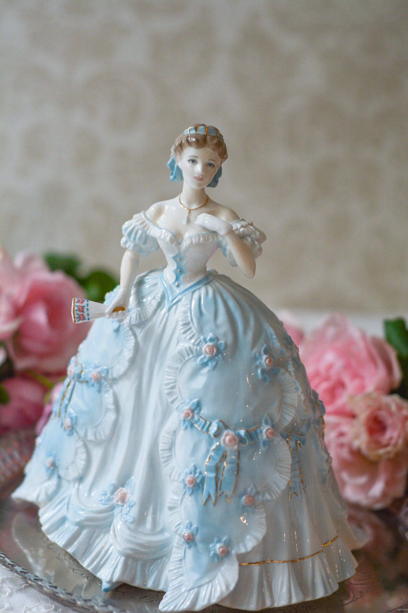The First Quadrilleという題名のとても可愛らしいロイヤルウースターのフィギュリンです。フィギュリンの題名の通り「初めての舞踏会」に出たご令嬢がモデルになっています。可愛らしいお顔のお嬢様ですが、表情には少し緊張している様子がうまく表現されていると思いませんか?ドレスは爽やかな水色に大きなリボンと薔薇の花がたくさんついていて、舞踏会デビューを華やかに飾っています。とても可愛らしく、美しいフィギュリンでテーブルやお部屋に花を添えてくれます。
