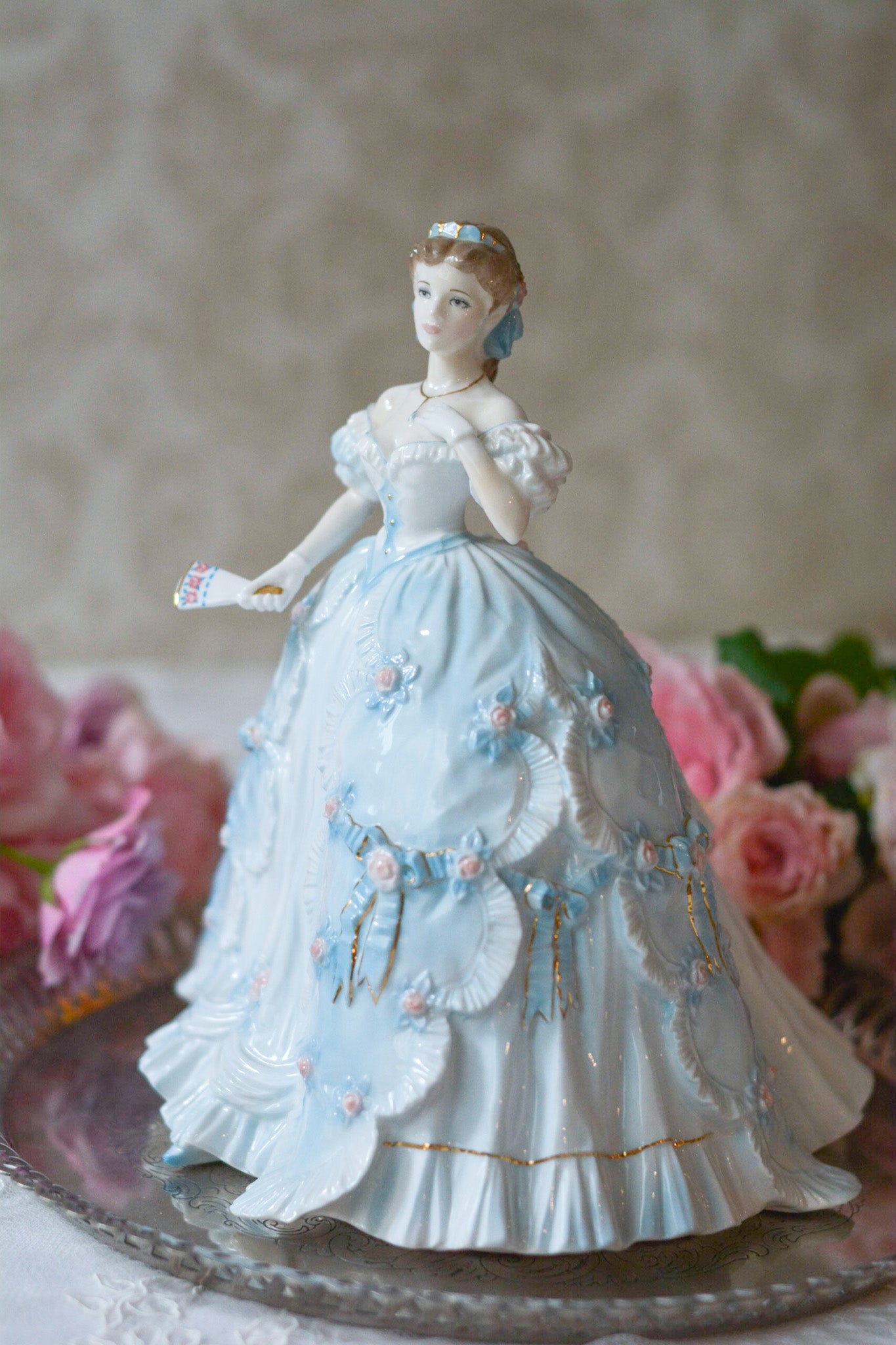 The First Quadrilleという題名のとても可愛らしいロイヤルウースターのフィギュリンです。フィギュリンの題名の通り「初めての舞踏会」に出たご令嬢がモデルになっています。可愛らしいお顔のお嬢様ですが、表情には少し緊張している様子がうまく表現されていると思いませんか?ドレスは爽やかな水色に大きなリボンと薔薇の花がたくさんついていて、舞踏会デビューを華やかに飾っています。とても可愛らしく、美しいフィギュリンでテーブルやお部屋に花を添えてくれます。