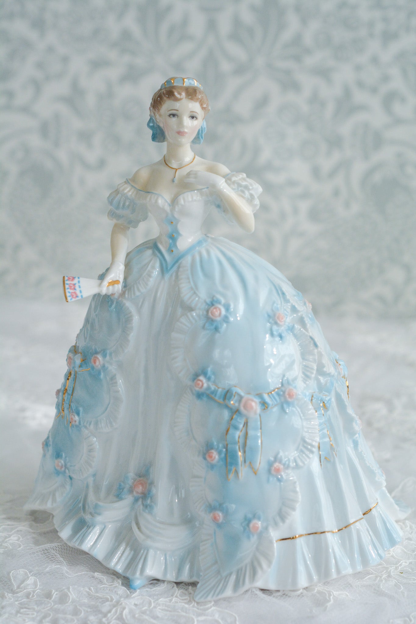 The First Quadrilleという題名のとても可愛らしいロイヤルウースターのフィギュリンです。フィギュリンの題名の通り「初めての舞踏会」に出たご令嬢がモデルになっています。可愛らしいお顔のお嬢様ですが、表情には少し緊張している様子がうまく表現されていると思いませんか?ドレスは爽やかな水色に大きなリボンと薔薇の花がたくさんついていて、舞踏会デビューを華やかに飾っています。とても可愛らしく、美しいフィギュリンでテーブルやお部屋に花を添えてくれます。