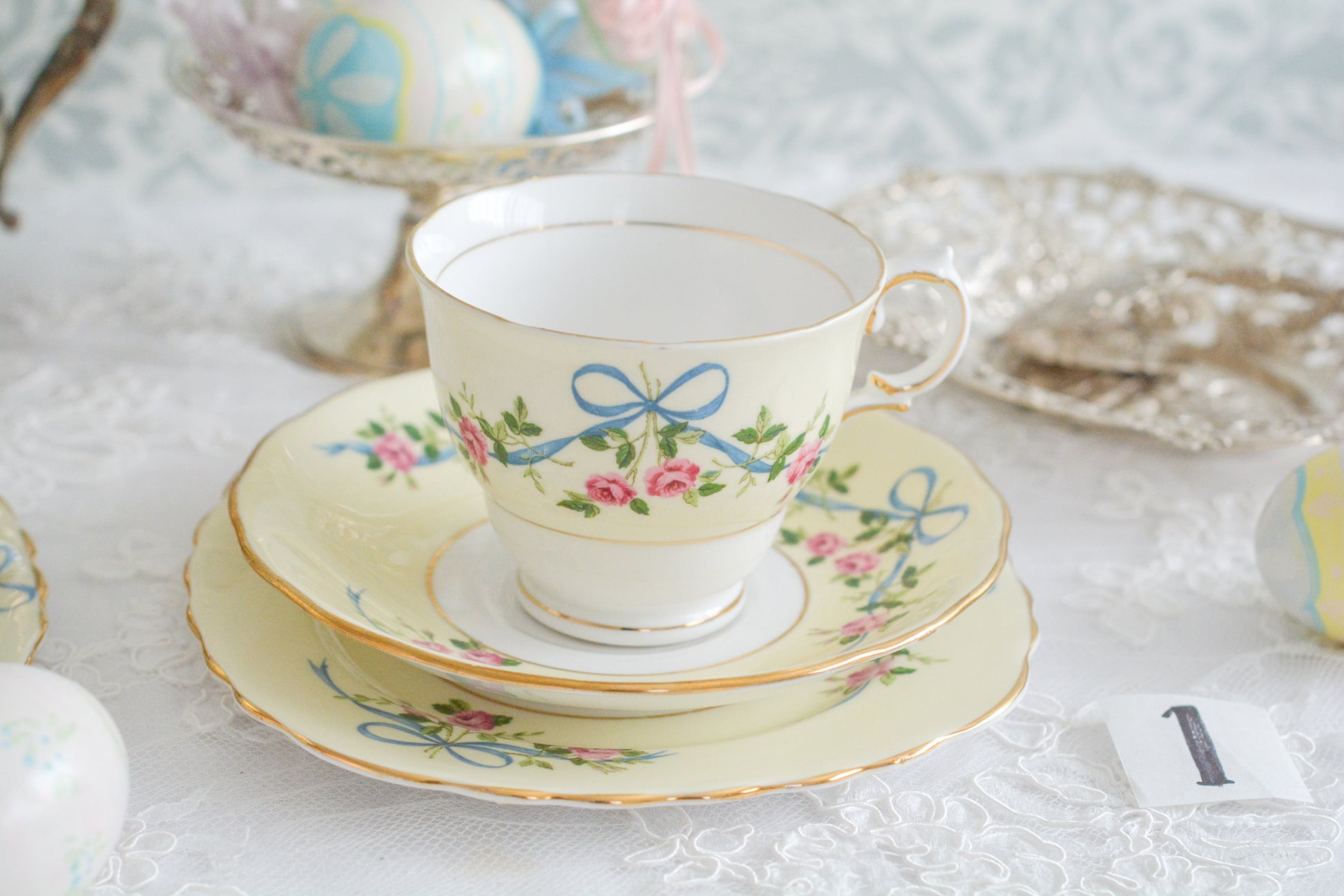 コルクラフ(Colclough)の可愛らしいティートリオ。コルクラフは1890年にハーバード・ジョセフ・コルクラフ氏が創業したメーカで、1940年代頃まで続いていました。コルクラフの中でもこのリボンの絵柄は人気で入手困難なお品です。クリーム色にブルーリボンと小さなバラの模様がとっても可愛らしいデザインです。パステルカラーがイースターや春のティータイムにもぴったりですね!
