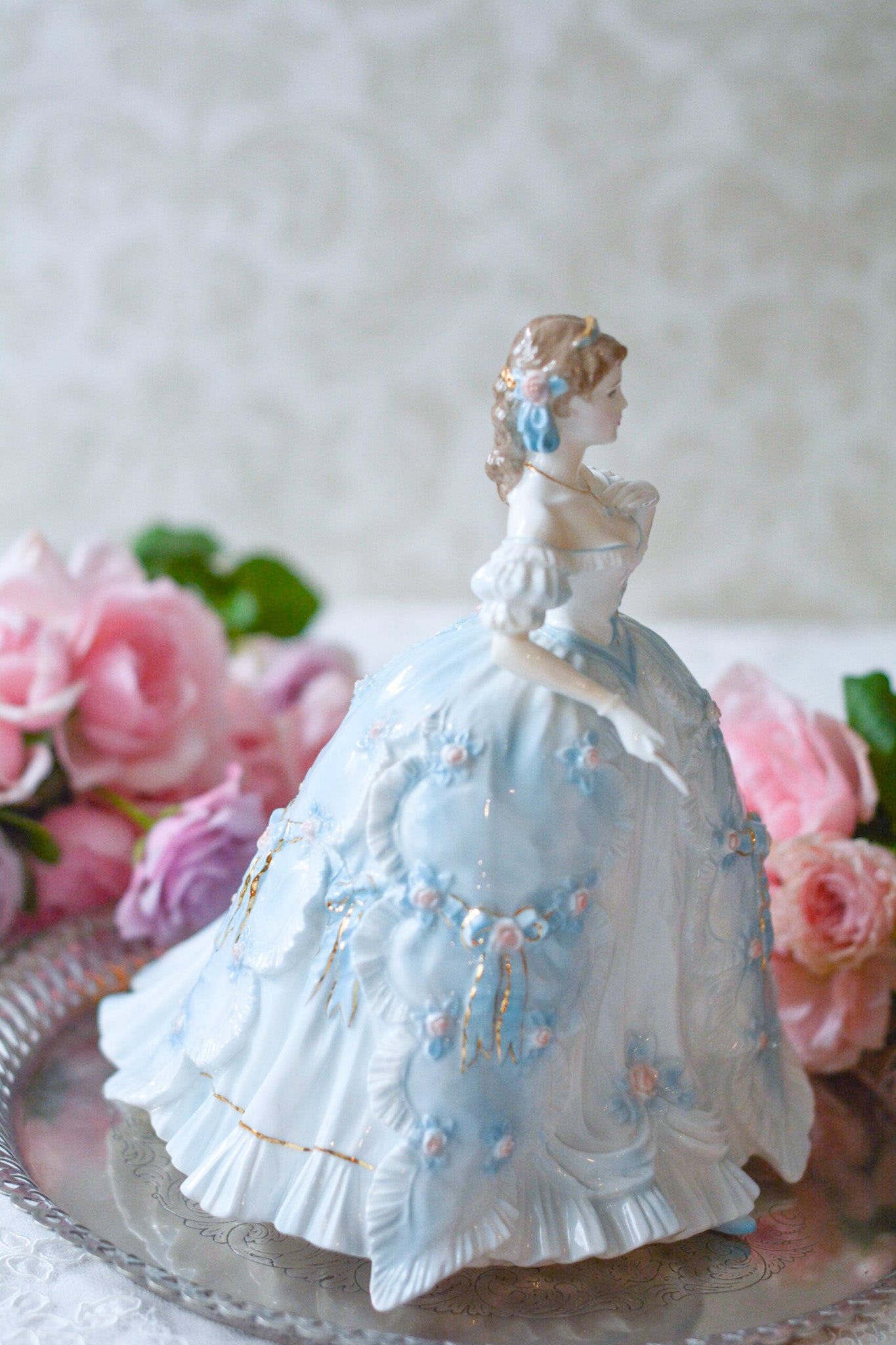 The First Quadrilleという題名のとても可愛らしいロイヤルウースターのフィギュリンです。フィギュリンの題名の通り「初めての舞踏会」に出たご令嬢がモデルになっています。可愛らしいお顔のお嬢様ですが、表情には少し緊張している様子がうまく表現されていると思いませんか?ドレスは爽やかな水色に大きなリボンと薔薇の花がたくさんついていて、舞踏会デビューを華やかに飾っています。とても可愛らしく、美しいフィギュリンでテーブルやお部屋に花を添えてくれます。