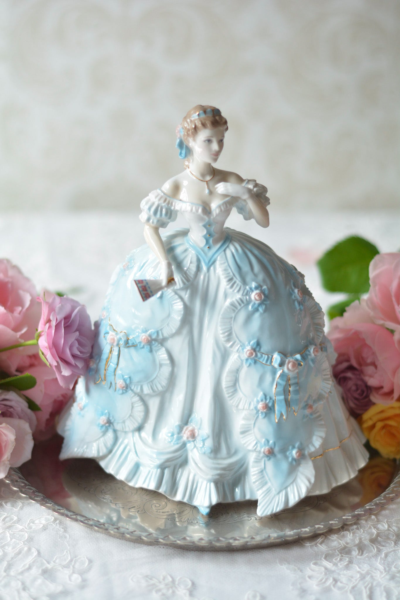 The First Quadrilleという題名のとても可愛らしいロイヤルウースターのフィギュリンです。フィギュリンの題名の通り「初めての舞踏会」に出たご令嬢がモデルになっています。可愛らしいお顔のお嬢様ですが、表情には少し緊張している様子がうまく表現されていると思いませんか?ドレスは爽やかな水色に大きなリボンと薔薇の花がたくさんついていて、舞踏会デビューを華やかに飾っています。とても可愛らしく、美しいフィギュリンでテーブルやお部屋に花を添えてくれます。