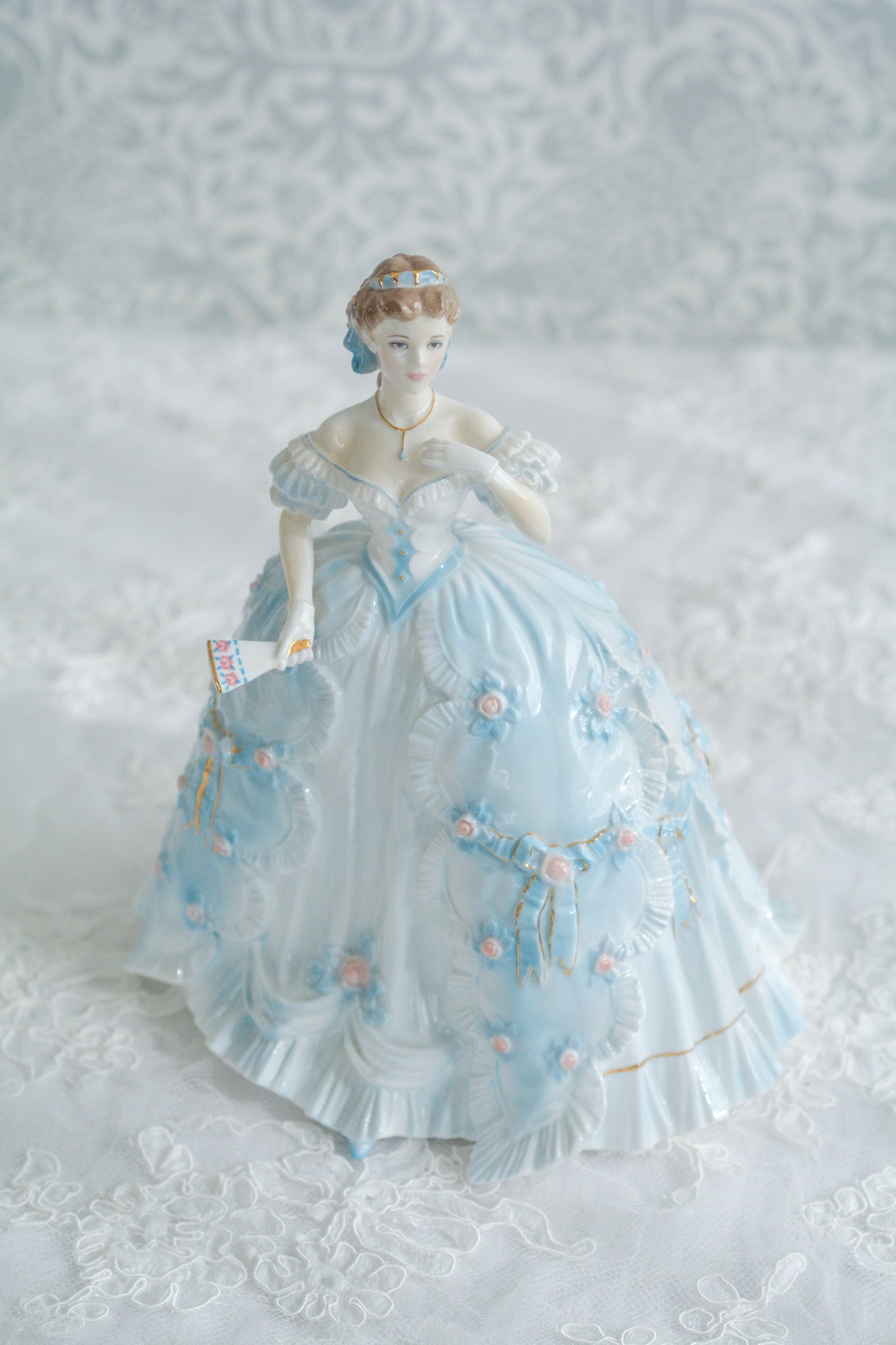 The First Quadrilleという題名のとても可愛らしいロイヤルウースターのフィギュリンです。フィギュリンの題名の通り「初めての舞踏会」に出たご令嬢がモデルになっています。可愛らしいお顔のお嬢様ですが、表情には少し緊張している様子がうまく表現されていると思いませんか?ドレスは爽やかな水色に大きなリボンと薔薇の花がたくさんついていて、舞踏会デビューを華やかに飾っています。とても可愛らしく、美しいフィギュリンでテーブルやお部屋に花を添えてくれます。