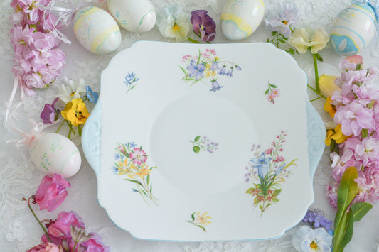 シェリーのワイルドフラワーシリーズの可愛らしいB&Bプレート(ブレッド&バタープレート)。イギリスの色とりどりの野草が散りばめられていて、パステルブルーの縁取りとハンドルが爽やかなお品です。春のティータイムやアフタヌーンティーにぴったりですね。イースターのテーブルコーディネートにもおすすめです!サインドイッチや焼き菓子、スイーツなど盛り付けてお楽しみください。