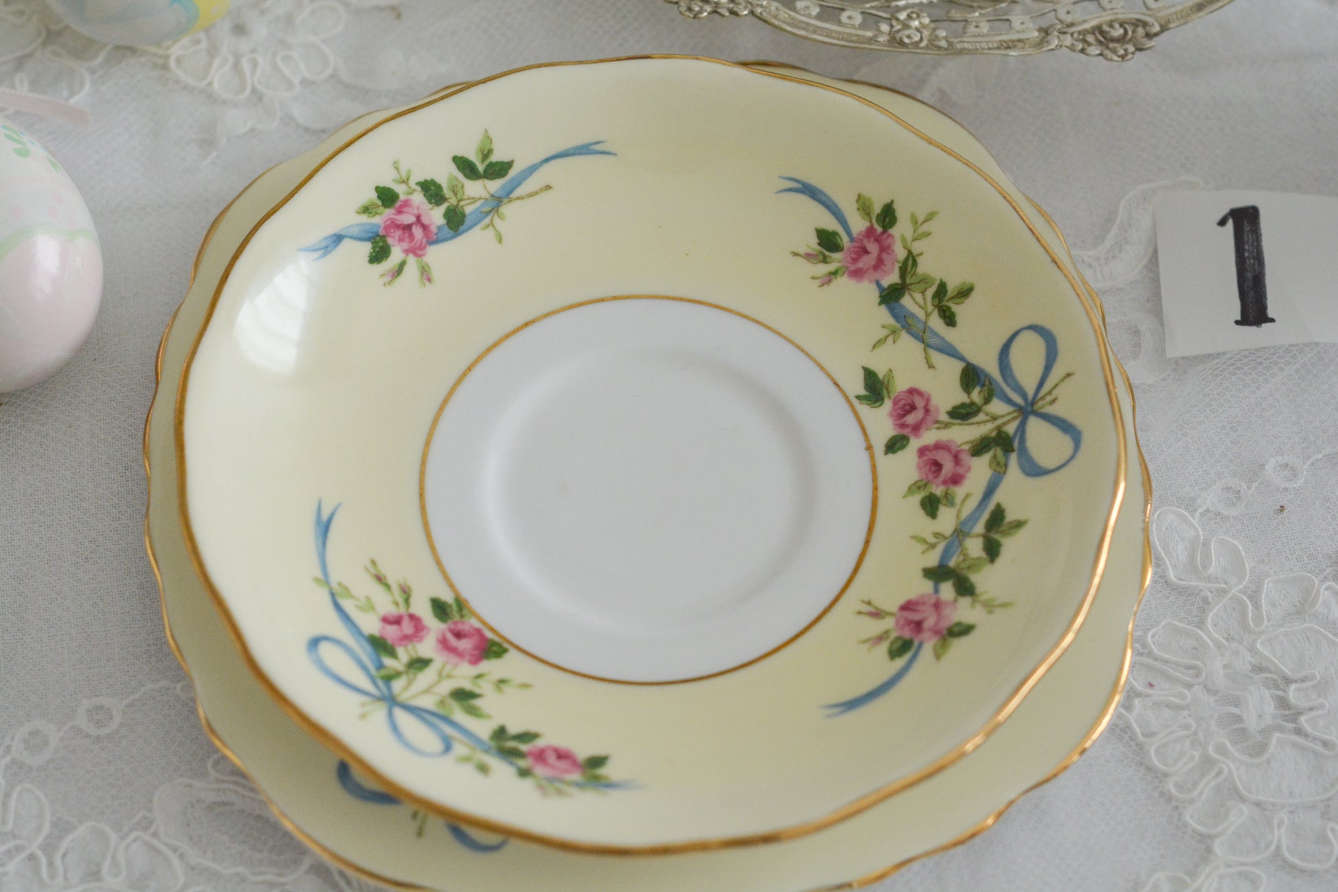 コルクラフ(Colclough)の可愛らしいティートリオ。コルクラフは1890年にハーバード・ジョセフ・コルクラフ氏が創業したメーカで、1940年代頃まで続いていました。コルクラフの中でもこのリボンの絵柄は人気で入手困難なお品です。クリーム色にブルーリボンと小さなバラの模様がとっても可愛らしいデザインです。パステルカラーがイースターや春のティータイムにもぴったりですね!