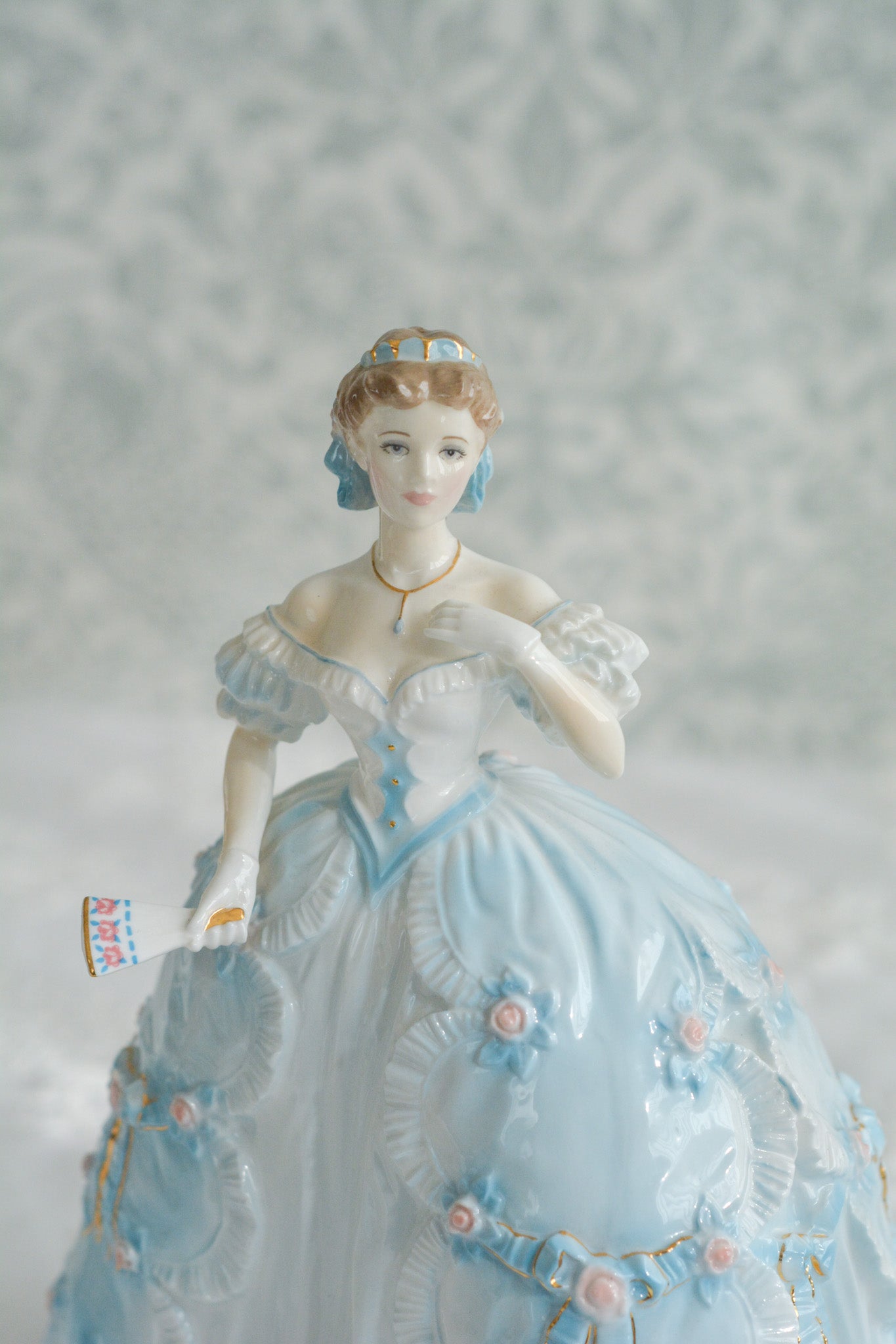 The First Quadrilleという題名のとても可愛らしいロイヤルウースターのフィギュリンです。フィギュリンの題名の通り「初めての舞踏会」に出たご令嬢がモデルになっています。可愛らしいお顔のお嬢様ですが、表情には少し緊張している様子がうまく表現されていると思いませんか?ドレスは爽やかな水色に大きなリボンと薔薇の花がたくさんついていて、舞踏会デビューを華やかに飾っています。とても可愛らしく、美しいフィギュリンでテーブルやお部屋に花を添えてくれます。