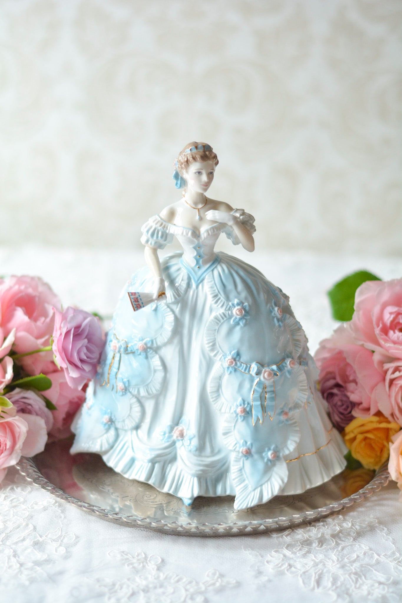 The First Quadrilleという題名のとても可愛らしいロイヤルウースターのフィギュリンです。フィギュリンの題名の通り「初めての舞踏会」に出たご令嬢がモデルになっています。可愛らしいお顔のお嬢様ですが、表情には少し緊張している様子がうまく表現されていると思いませんか?ドレスは爽やかな水色に大きなリボンと薔薇の花がたくさんついていて、舞踏会デビューを華やかに飾っています。とても可愛らしく、美しいフィギュリンでテーブルやお部屋に花を添えてくれます。