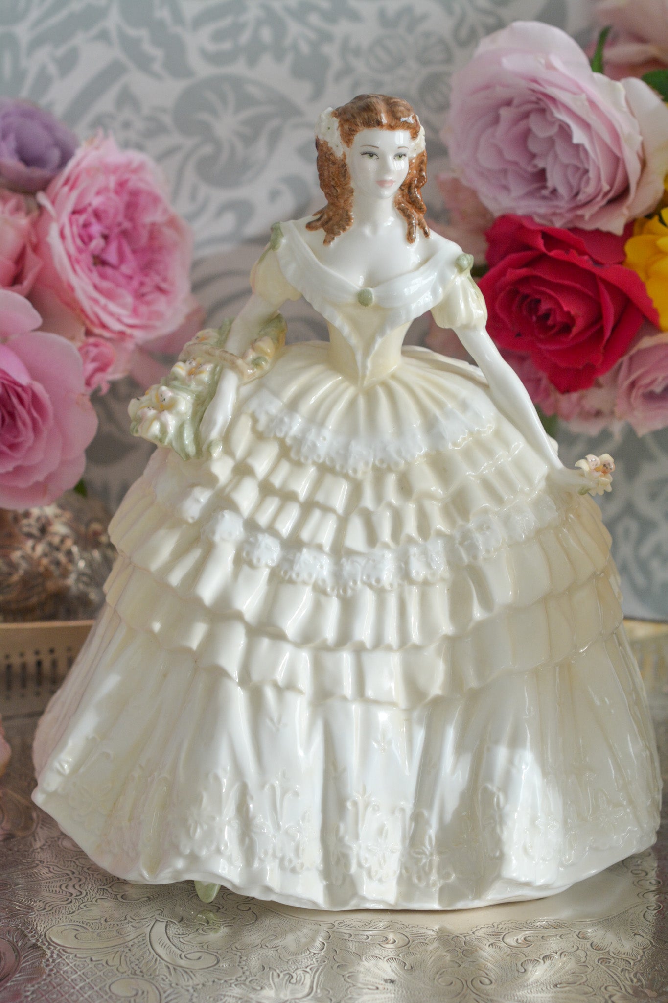 コールポートの人気フィギュリン、「The Four Flowers Collection」。名前の通り、「リリー、ローズ、カーネション、アイリス」の4つのお花がモチーフのフィギュリンシリーズです。 その中でも、リリーはアイリスと並び入手困難なお品です。  バスケットいっぱいのリリーと左手には一輪のリリーの花。ドレスはホワイトに淡いイエローのフリルとグリーンのリボンがあしらわれています。 柔らかな表情がとても可愛らしいレディのフィギュリンです。